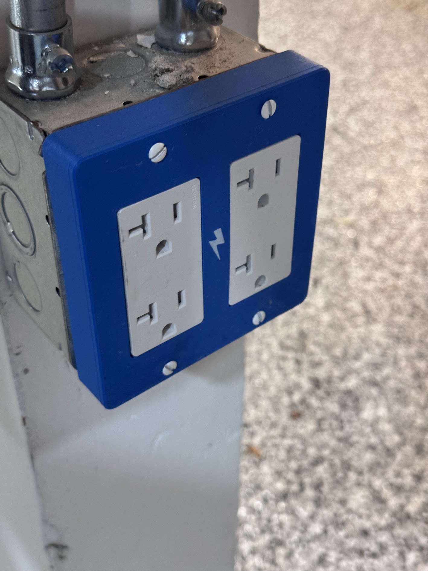 The blue 3D-printed replacement outlet cover installed on the metal box